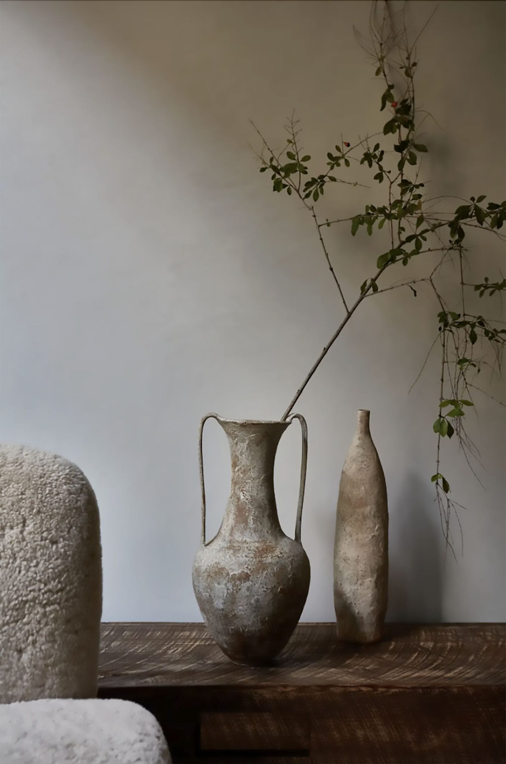 Minimalist vignette with weathered ceramic vases and branch on rustic wooden table