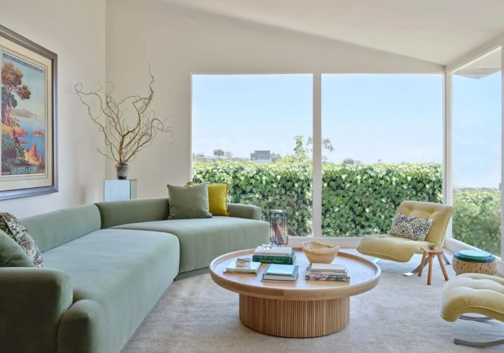 Bright living room with green sectional sofa and large windows overlooking greenery